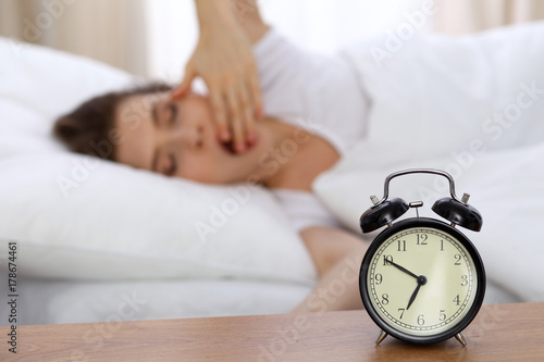 Beautiful sleeping woman resting in bed and trying to wake up with alarm clock