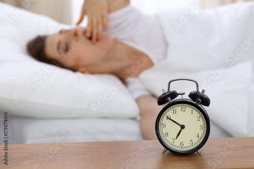 Beautiful sleeping woman resting in bed and trying to wake up with alarm clock