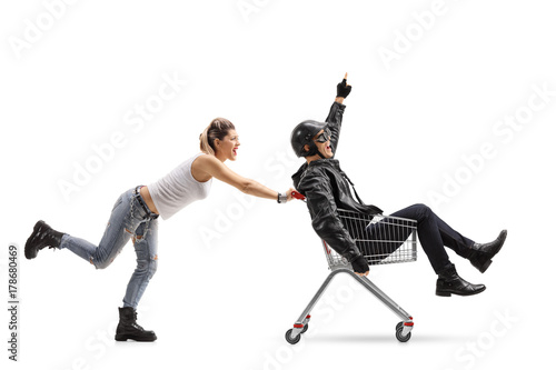 Punk girl pushing a shopping cart with a biker riding inside and pointing up