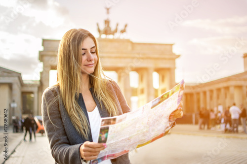 Beautiful young woman looking at map guide while standing in front of Brandenburg gate at sunset.