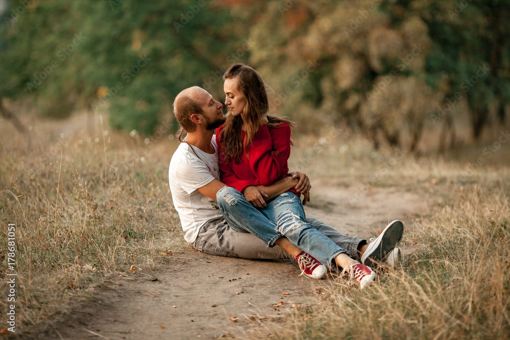 Enamored couple sits and embraces on forest path.