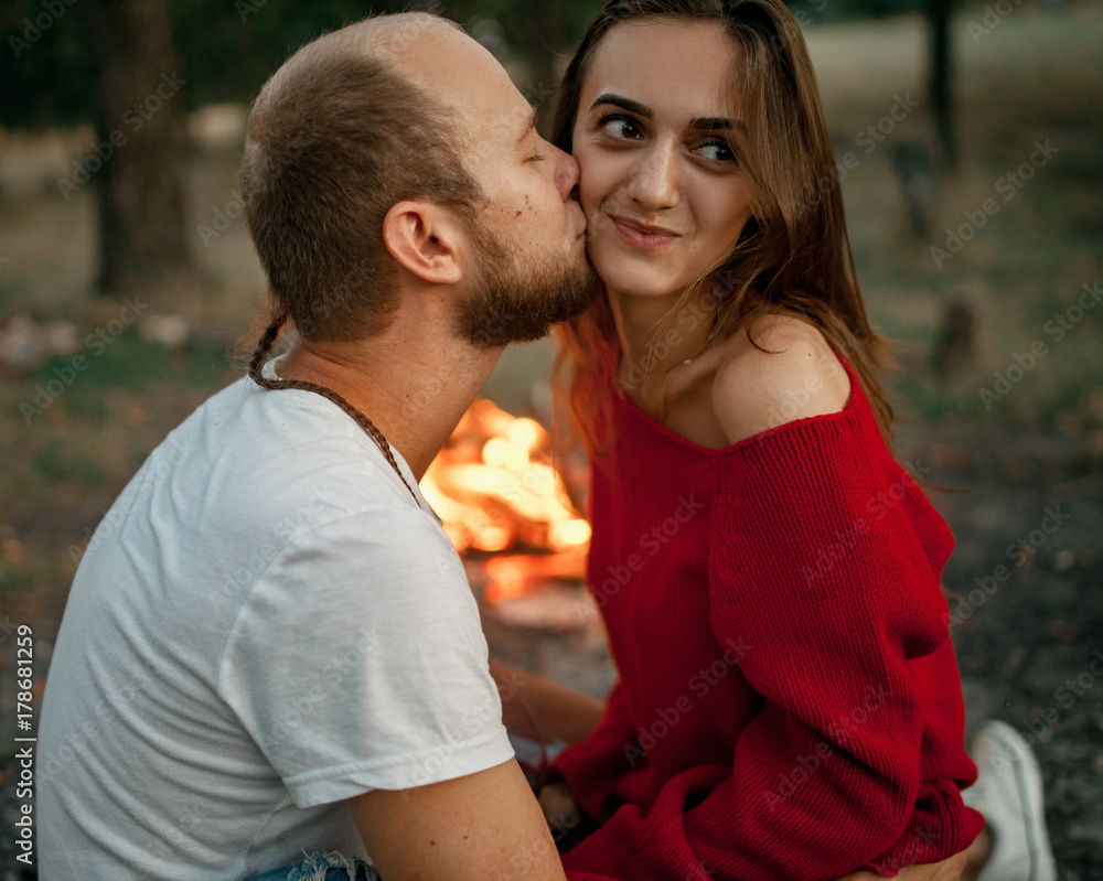 Enamored couple sits and kisses on picnic in forest on bonfire flame background. Enamored couple sits and kisses on picnic in forest on bonfire flame background.