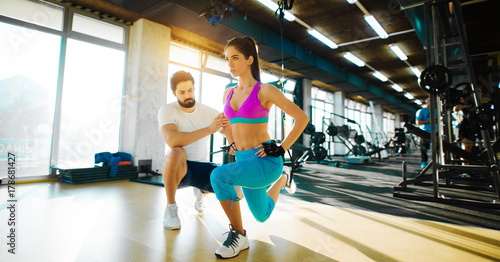 Fitness flexible girl doing leg stretching with rope from top and help from a personal trainer in the gym.