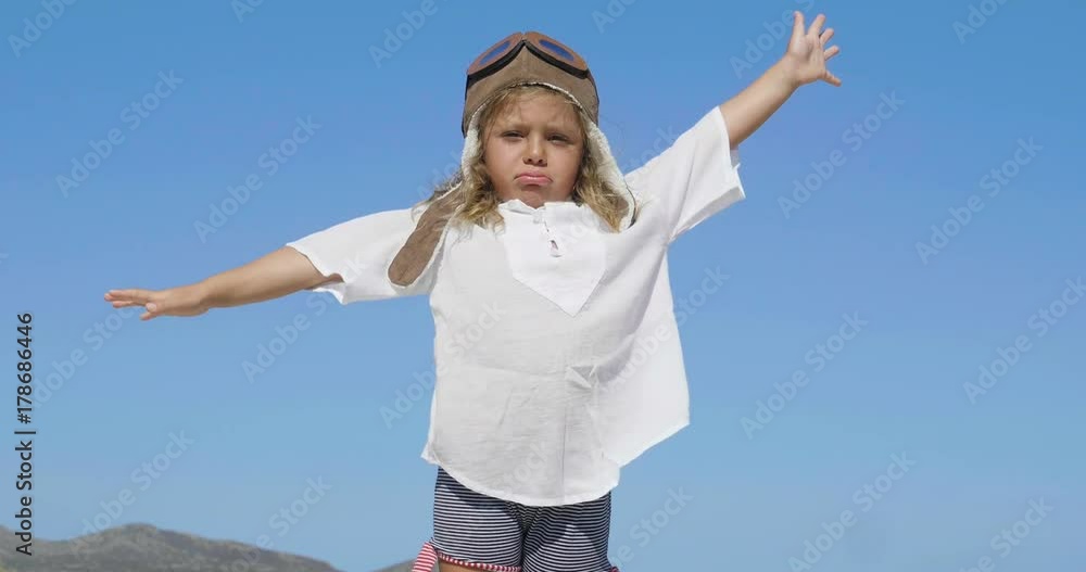 Little happy girl in aviator's cap smiling and playing, in white T-shirt, blue sky background. Little happy girl in aviator's cap smiling and playing, in white T-shirt, blue sky background.