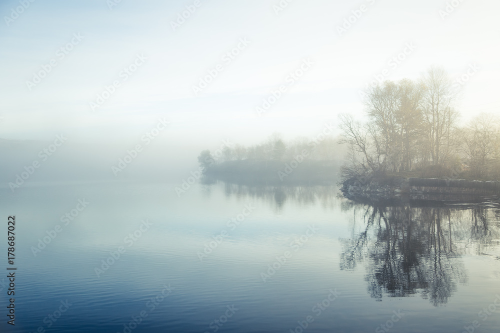 A beautiful, colorful misty morning in Norway at the lake. Tree reflections in the water. Misty autumn landscape. Calm nordic scenery.