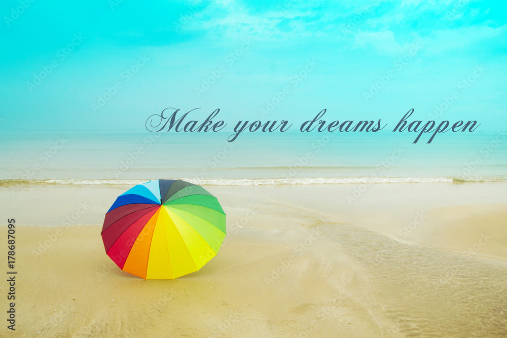 Inspirational motivation quote MAKE YOUR DREAMS HAPPEN with colorful umbrella on the beach