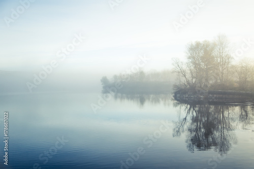 A beautiful, colorful misty morning in Norway at the lake. Tree reflections in the water. Misty autumn landscape. Calm nordic scenery.