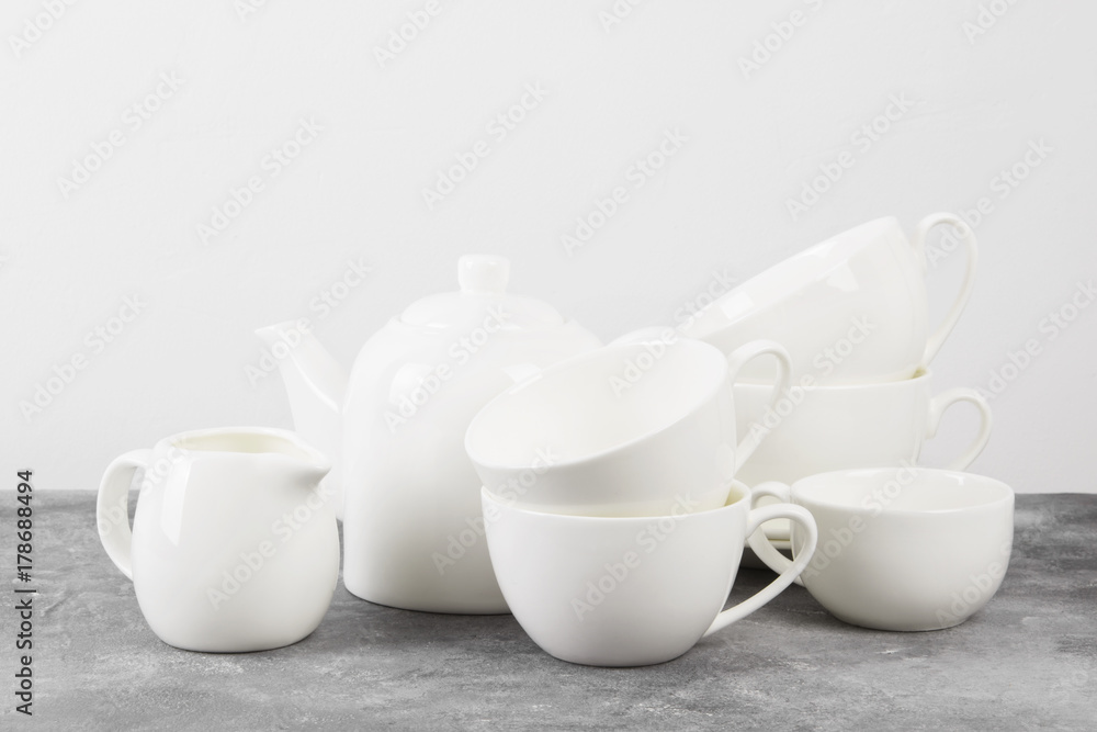 Clean white tableware (teapot, cups, saucers) on a gray background Clean white tableware (teapot, cups, saucers) on a gray background