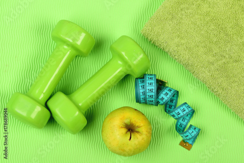 Barbells, apple and tape measure near green towel