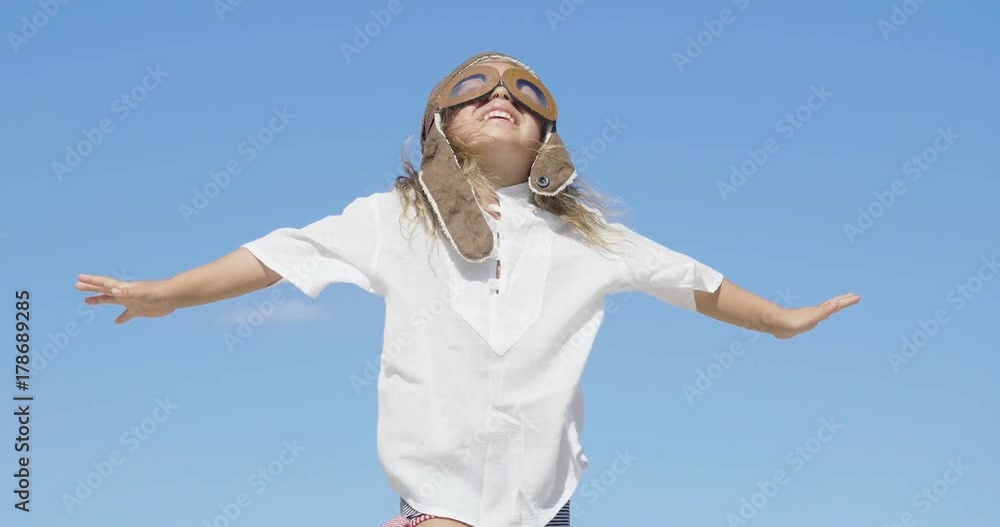 Little happy girl in aviator's cap smiling and playing, in white T-shirt, blue sky background. Little happy girl in aviator's cap smiling and playing, in white T-shirt, blue sky background.