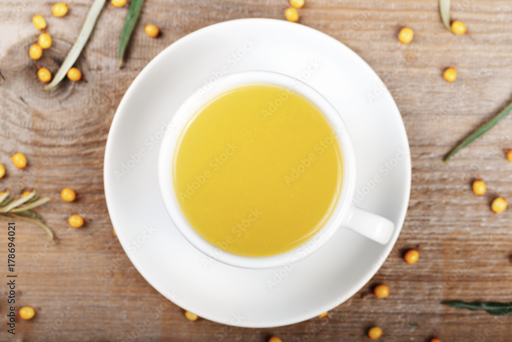 sea-buckthorn tea in a white cup on the table. near lay berries of sea-buckthorn