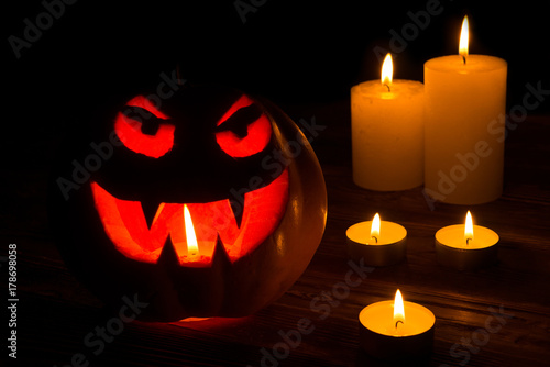 Carved Halloween pumpkin lights inside with flame on a black background. Celebration of Halloween. Pumpkin head jack lantern with burning candles in the dark room