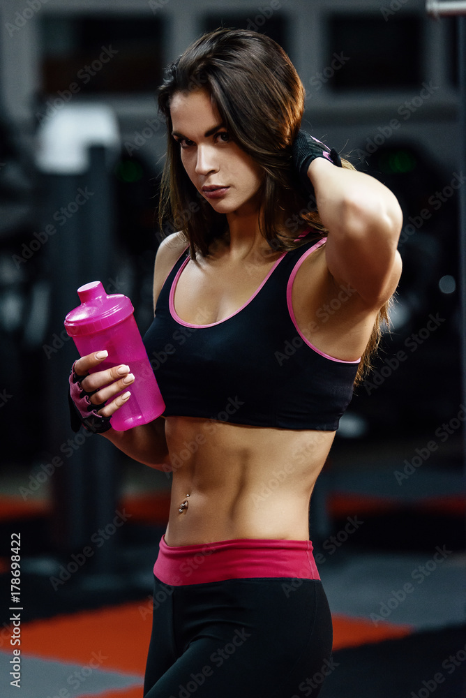 Athletic young woman after hard workout at gym. Fitness girl holds shaker  with sportive nutrition. Stock Photo