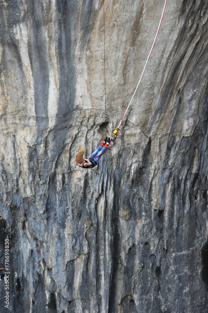 Fototapeta premium Bungee jumping in Prohodna Cave, Bulgaria. Young woman with long blond hair hanging on a cord, the dark rocks of the cave seen at background