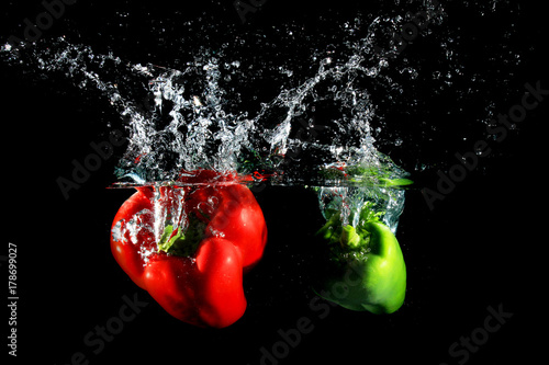 Red and green peppers falling into water, on black background
