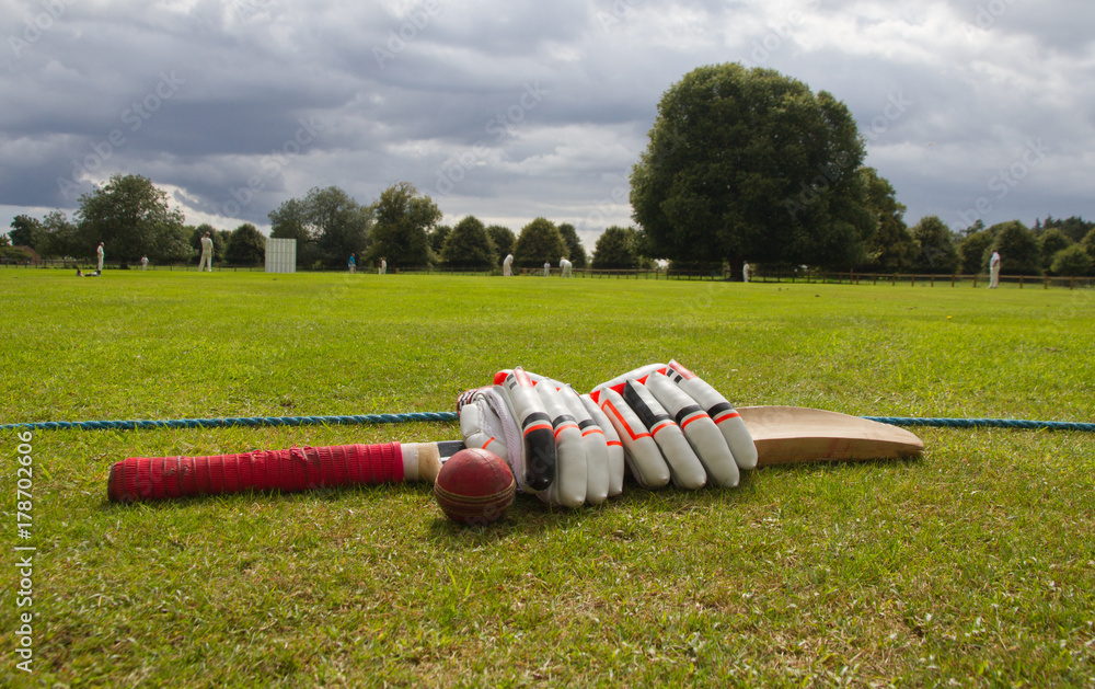 Cricket bat and gloves on the boundary line waiting to be used in English village game.