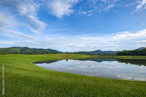 Scenic View Of Grassy Field near lake with cloudy sky