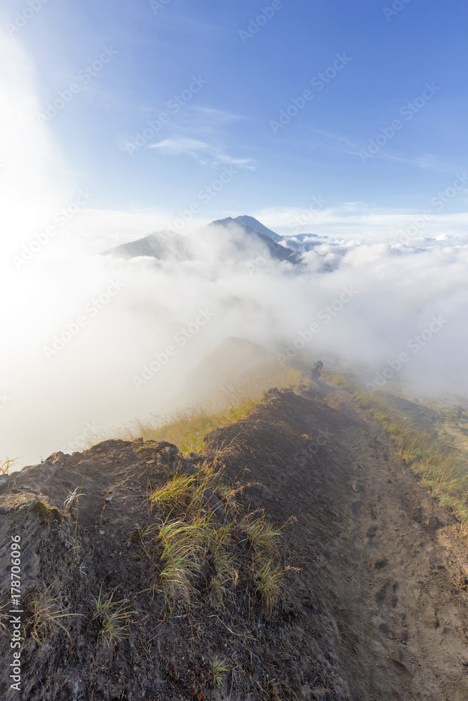 A trail leads into the morning mist which also hides Mount Agung in the distance in Bali, Indonesia.