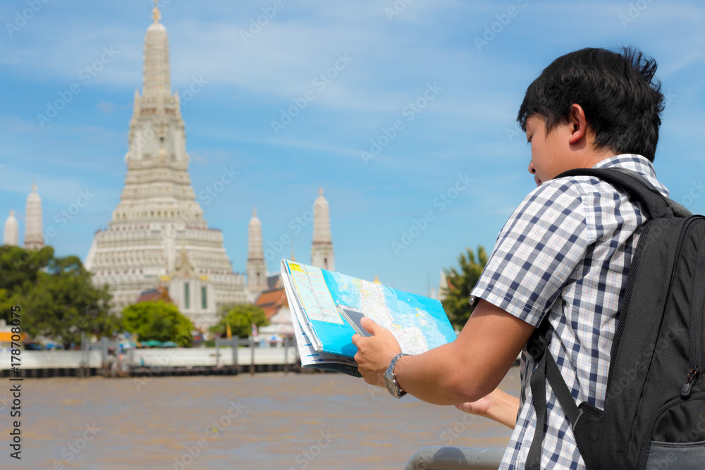 Man stand holding a map and a mobile phone on the river and Wat Arun in Thailand.