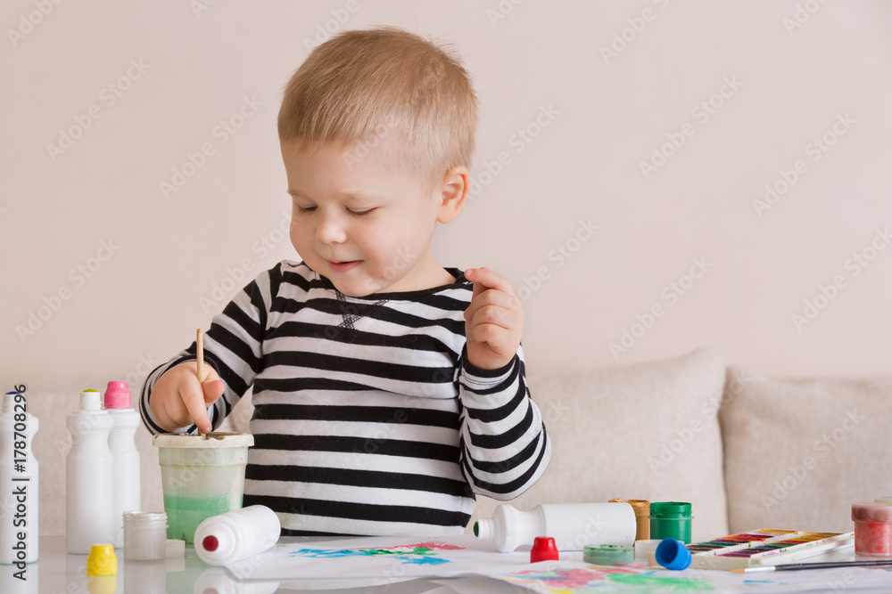 Portrait of smiling cute toddler boy drawing at home with color paints and brush. Creative child having fun. Educational and learning concept Portrait of smiling cute toddler boy drawing at home with color paints and brush. Creative child having fun. Educational and learning concept