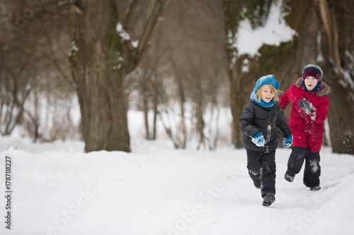 Portrait of adorable little kid boys running on snow and playing with snow outdoors in the park. Children in warm clothes walking and having fun on a windy winter day.
