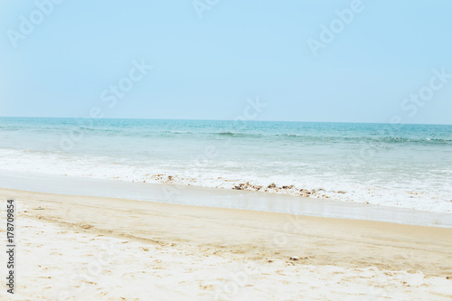 Tropical sandy beach, view of the sea with waves and sunny sky.