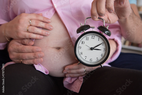 Husband hugs pregnant wife and keeps alarm clock in hand