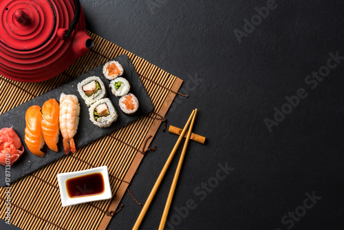 Set of sushi with wasabi, soy sauce and teapot on black stone background. Top view