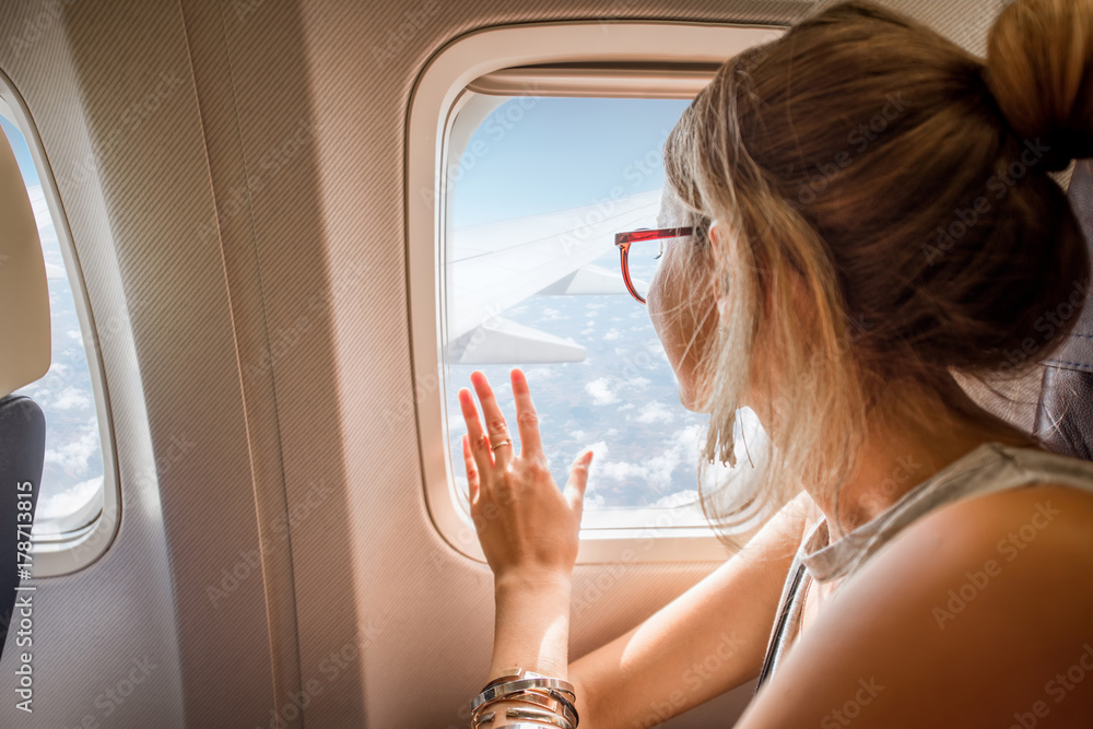 Naklejka premium Młoda kobieta cieszy się widok przez okno samolotu obsiadanie podczas lota w samolocie