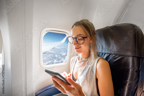 Young woman sitting with phone on the aircraft seat near the window during the flight in the airplane photo