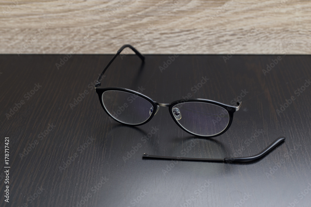 Old black glasses with broken legs against black background. Old black glasses with broken legs against black background.