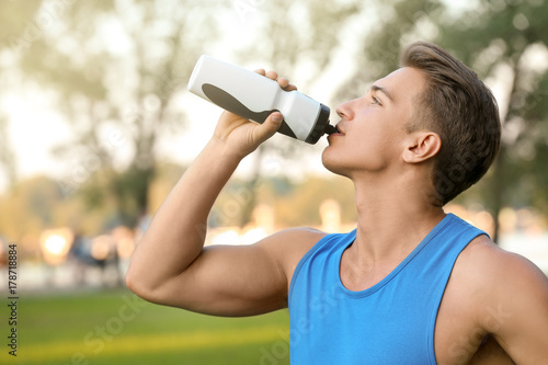 Fototapeta Naklejka Na Ścianę i Meble -  Sporty young man drinking water outdoors