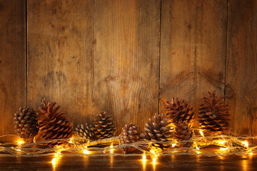Holiday image with Christmas golden garland lights and pine cones over wooden background