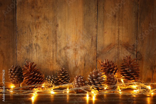 Holiday image with Christmas golden garland lights and pine cones over wooden background photo