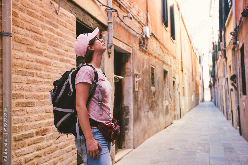 the tourist girl in the caucasian stands on an old deserted street in venice in italy and looks up in the summer