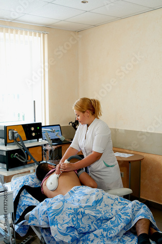 Female doctor does transcranial magnetic stimulation the man with a broken spine. Physiotherapy. Electrotherapeutic treatment of the back. photo