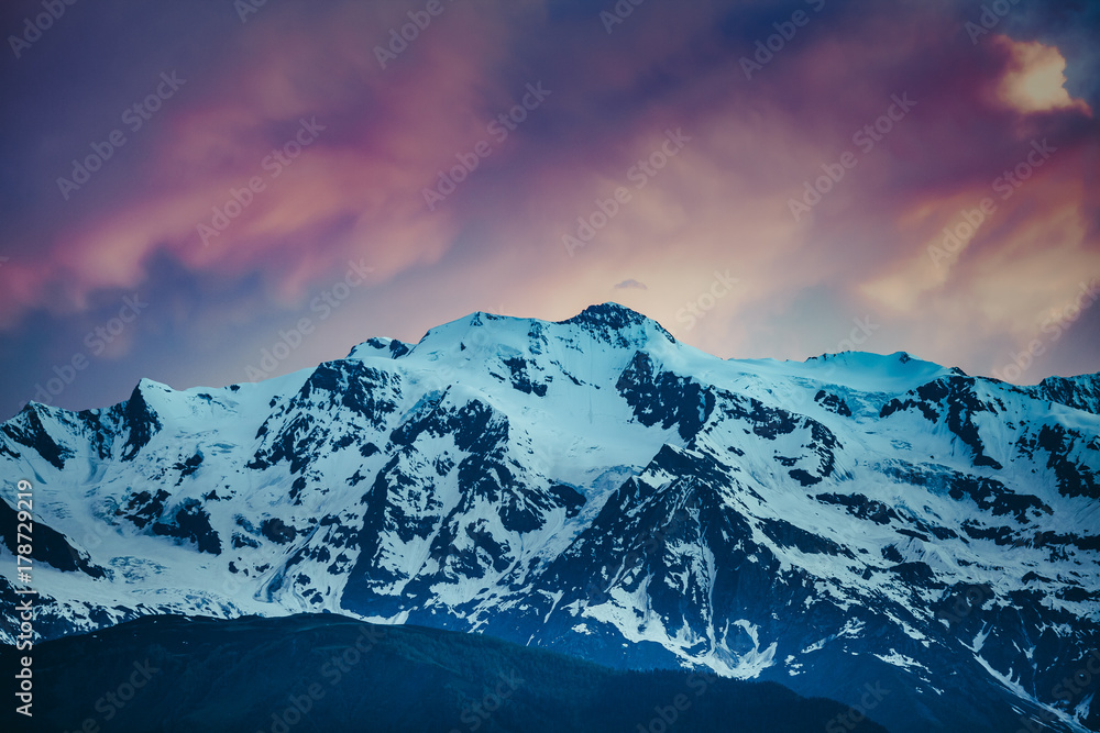 Beautiful colorful sunset over the snowy mountain range. Nature landscape. Dramatic overcast pink sky. Holiday, travel, sport, recreation. Kazbegi National Park, Gergeti, Georgia. Retro toning filter