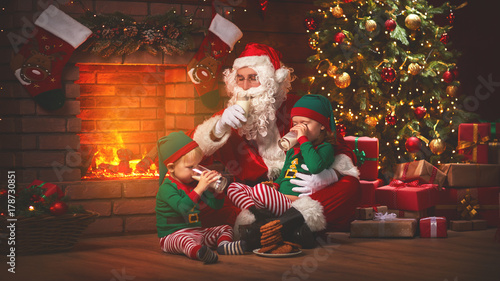 Christmas. Santa Claus with Elves Drink Milk and Eat Cookies