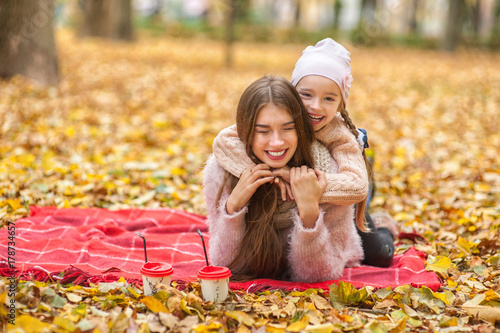 .Beautiful mother and daughter lie in autumn leaves in a park or forest communicate  laugh  have fun  mother s day