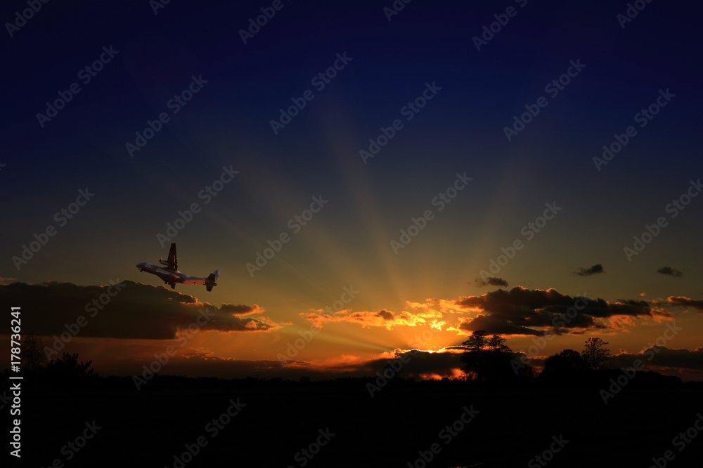 Fototapeta premium Wojskowy samolot transportowy wznosi się w powietrze przy zachodzie słońca.