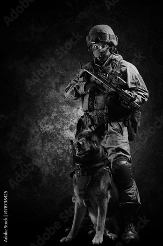 Obraz na plátně Armed soldier of a special unit with a machine gun stands with his shepherd