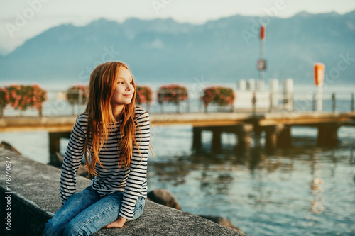 Cute little redheaded girl resting by lake Geneva at sunset, image taken in Lausanne, Switzerland