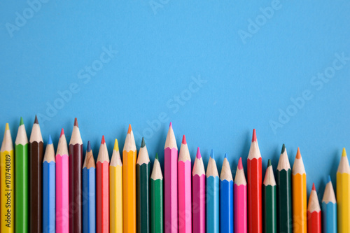 Colored crayons background. Many different colored pencils on blue background