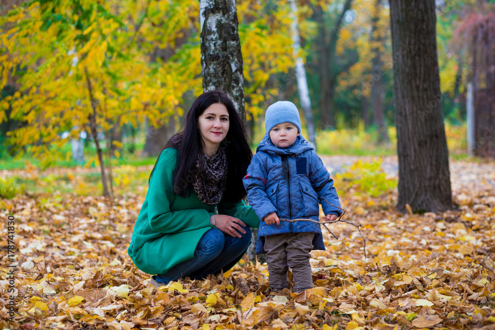 Mother with little son plays and smiles in park on background of colorful autumn fallen leaves Mother with little son plays and smiles in park on background of colorful autumn fallen leaves