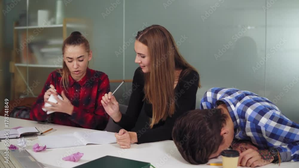 Group of tired workers in a creative start up work environment holding a project meeting in a conference room. They are discussing a project and crumpling papers, working hard before the deadline Group of tired workers in a creative start up work environment holding a project meeting in a conference room. They are discussing a project and crumpling papers, working hard before the deadline