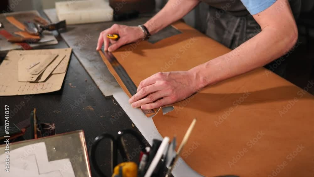 Close up shot of specialist working with leather in his workshop. He measures a piece of leather and cuts it with knife. Close up shot of specialist working with leather in his workshop. He measures a piece of leather and cuts it with knife.