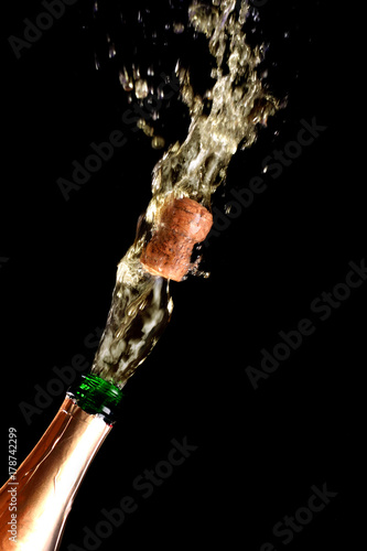Cork flies out of champagne bottle isolated on black background