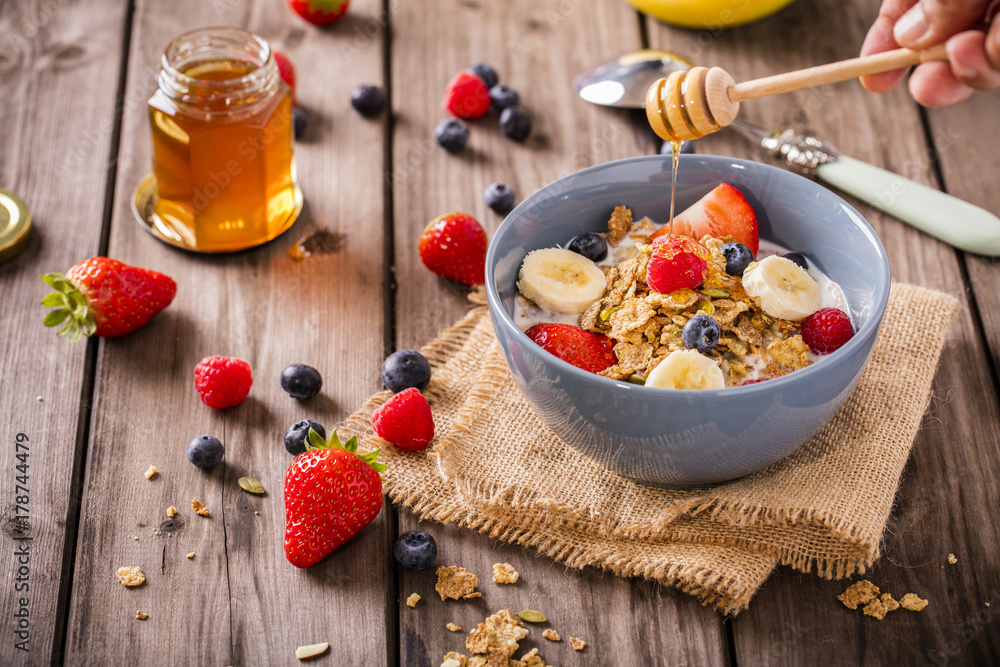 breakfast cereal shot on linen cloth wood boards angled view with raspberries blueberries sliced bananas strawberries with hand swirling honey landscape breakfast cereal shot on linen cloth wood boards angled view with raspberries blueberries sliced bananas strawberries with hand swirling honey landscape