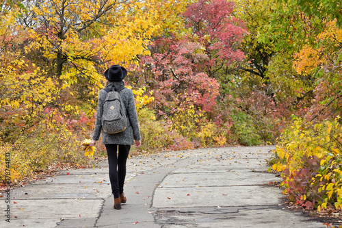 Girl in a hat walking in the autumn park. Bright foliage. Back view