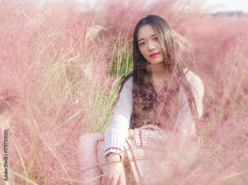 Portrait of beautiful young Chinese woman wearing white sweater sitting in the pink hairawn muhly field. photo